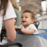 Happy baby sitting with mom at table outside, showing the Boppy product of a 4 in one cover. This image is a composite showing a different design for the product.