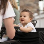 Happy baby sitting with mom at table outside, showing the Boppy product of a 4 in one cover. This is the original photograph.