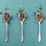 Product photography of loose tea on 3 spoons and teal background.