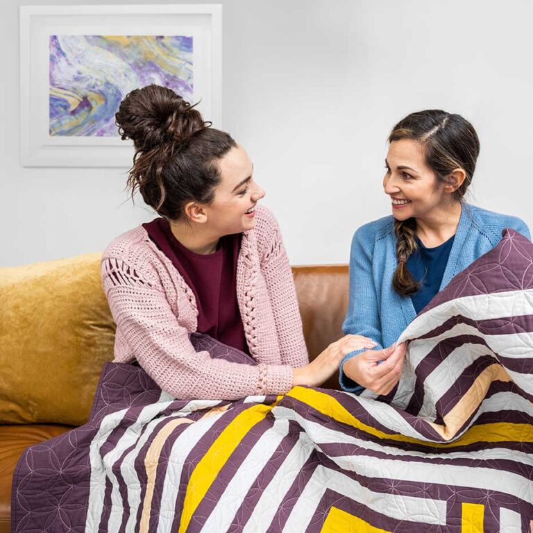 High end composite of women laughing as they look at hand made quilt.