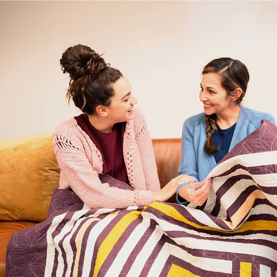 Product photography of women laughing as they look at hand made quilt, unedited.