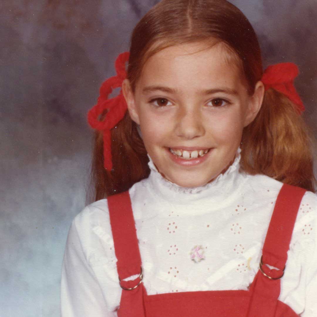 Child's vintage school headshot with girl in red jumper and pigtails.