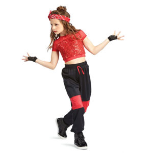Hip hop dancer posed with one foot in frontand the other pressed behind arms bent to the sides as though saying "what" and looking off camera.