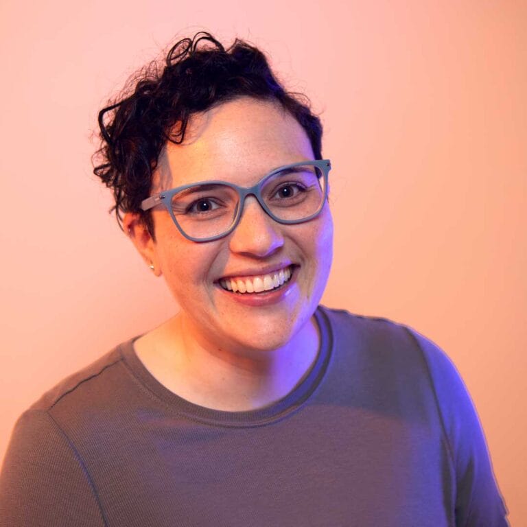 Headshot of Amber on a peach background with purple gel lights