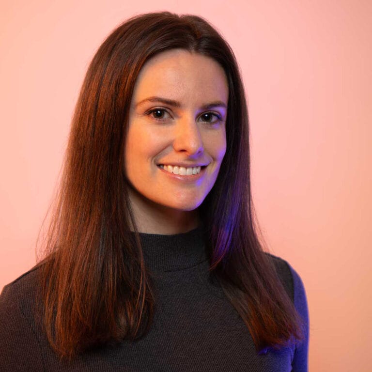 Headshot of Brooke on a peach background with purple gel lights