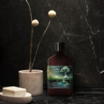 Photo composite of lotion bottle from Melt in a black marble bathroom setting.