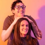 Amber leaning on Brooke's head in a colorful gel-lit set in orange and purple.