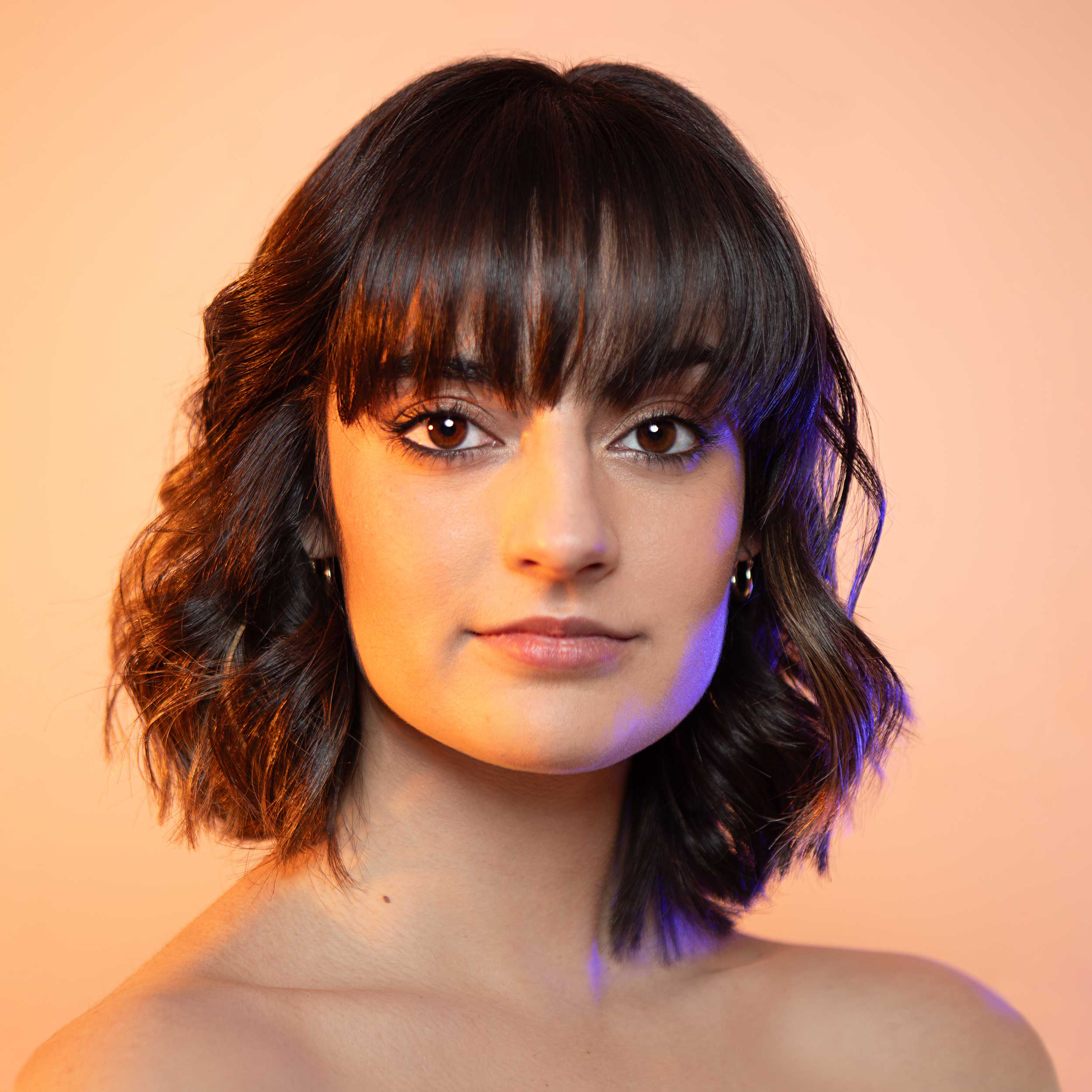 Headshot of an artist with colorful gel lights illuminating the edge of the face and a brightly colored orange background.