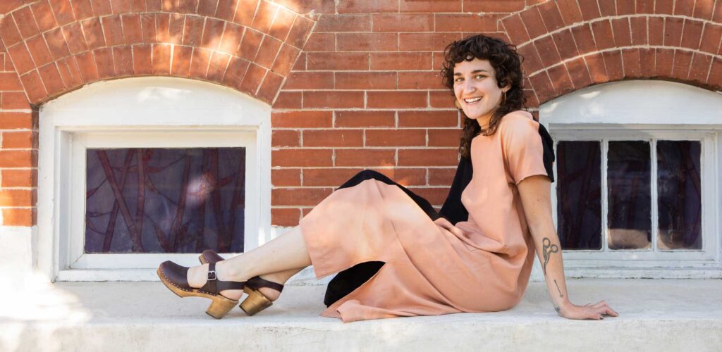 Woman modeling her self-made dress, sitting on a concrete sill in front of an old building