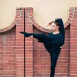 Dancer doing a bent leg hold against a brick wall on a pedestal