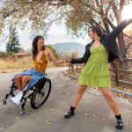 Dancer pair posed reaching outward, with the dancer in her wheelchair on a one wheel tilt