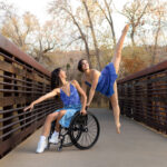 Dancing duet on a bridge, one in a wheelchair reaching out and the other leaping back