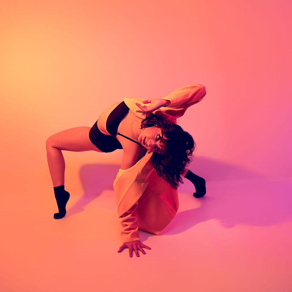 Contemporary dancer in a back arch leaning on the floor and looking back and downward, in an orange and purple gel set