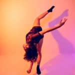 Dancer in a tilt with attitude leg, bent forward with purple and orange gels