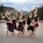 Dancers reaching in flowing motions against a mountain scape and stormy sky