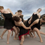 Dancers arching in outward poses against a mountain scape and stormy sky