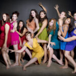 Dancers in rainbow dresses lined up against a black wall