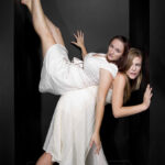 Dancers in a black corridor balancing against the walls while wearing white dresses