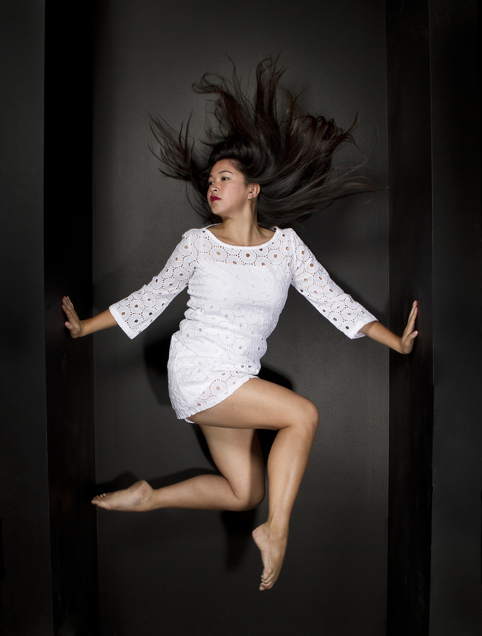 Dancer in white dress holding up on the walls as she jumps in an angled pose with her hair flying