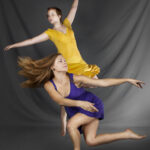 Dancers in yellow and purple dresses improvising poses on a grey background