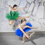 Dancers in matching poses, one lunging on the floor and one leaping in the air, wearing brightly colored tutus