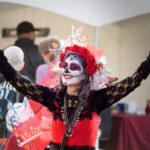 Magician with Dia De Los Muertos costume and makeup showing a trick