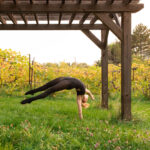 Dancer in a handstand extending backward under a pergola in a vineyard