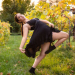 Dancer in a passe pose holding her dress while in the middle of a vineyard