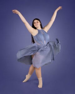 ballet dancer posed in b plus with arms raised throwing skirt on blue