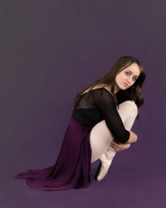 ballet dancer posed in over the toes on pointe holding legs on deep purple