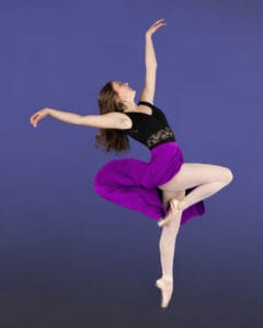 ballet dancer posed in passe side on pointe with skirt motion on blue