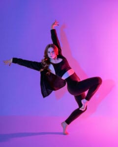 contemporary dancer posed in forced arch passe off balance on purple and pink