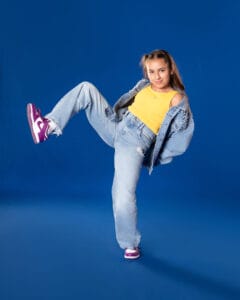 hip hop dancer posed in back lean with one leg lifted on blue