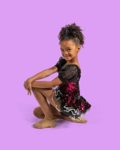 young jazz dancer posed kneeling to the side with hands on knee on magenta