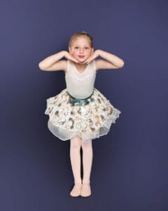 young ballet dancer posed leaning forward with hands under chin on deep blue