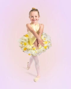 young ballet dancer posed in b plus with arms crossed in front on pink