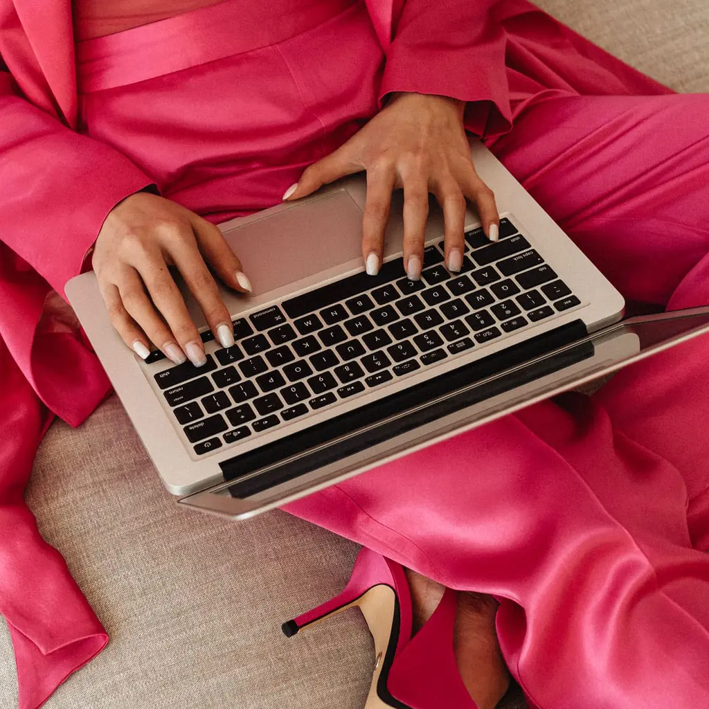 Elegant woman in pink suit working on laptop, emphasizing professional digital artistry.