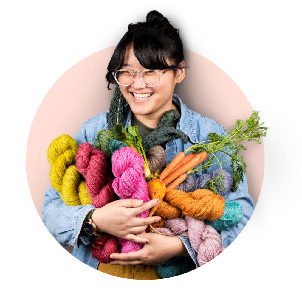 Vibrant yarn balls and fresh vegetables held by a smiling woman at Andrews Artistry.
