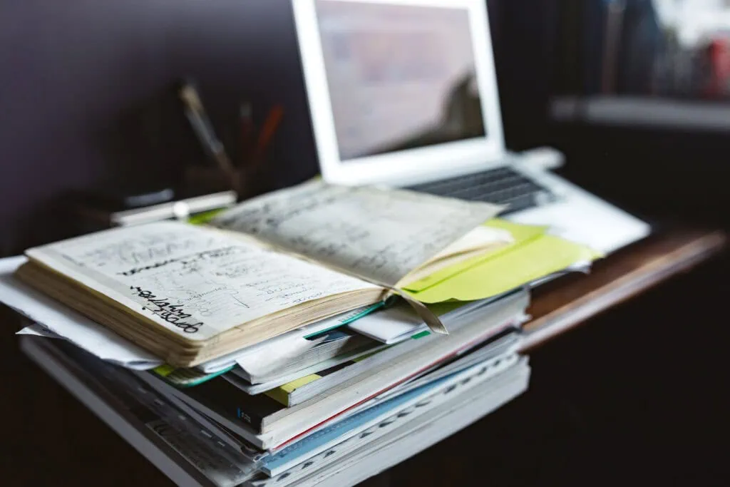 Notebooks and papers on a wooden desk with a laptop, workspace for creative projects or art design.